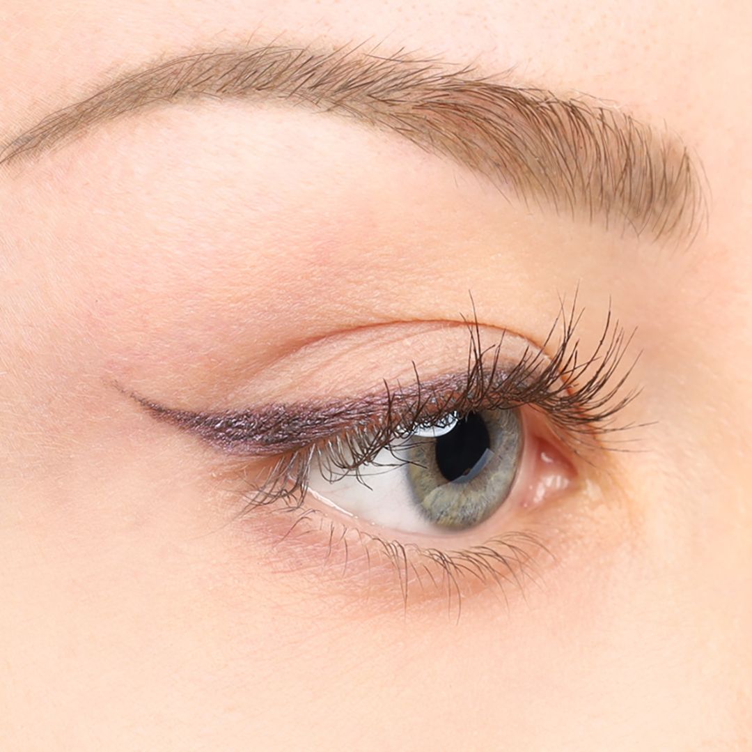 Nahaufnahme eines Auges mit lila Kajal-Eyeliner auf dem oberen Augenlid. Die Wimpern sind getuscht.