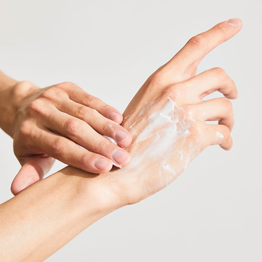 Hände, die eine Creme auf der Handfläche verteilen. Die Creme ist weiß und die Haut ist leicht gerötet.