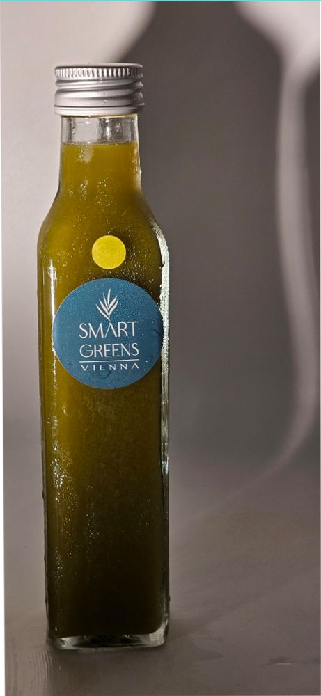Grüne Flüssigkeit in einer Glasflasche mit Schraubverschluss. Blaues Etikett mit "SMART GREENS VIENNA". Gelber Punkt.