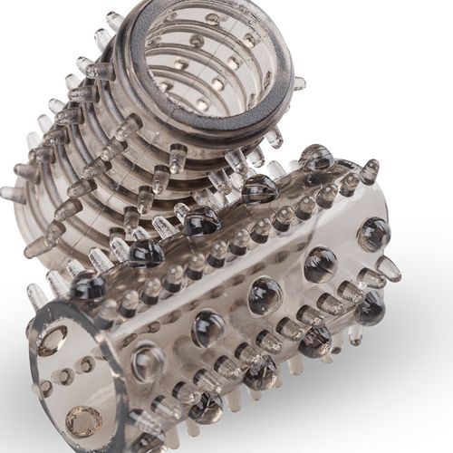 Nahaufnahme einer transparenten Silikon-Penishülle mit Noppen und einem Ring. Auf weißem Hintergrund.