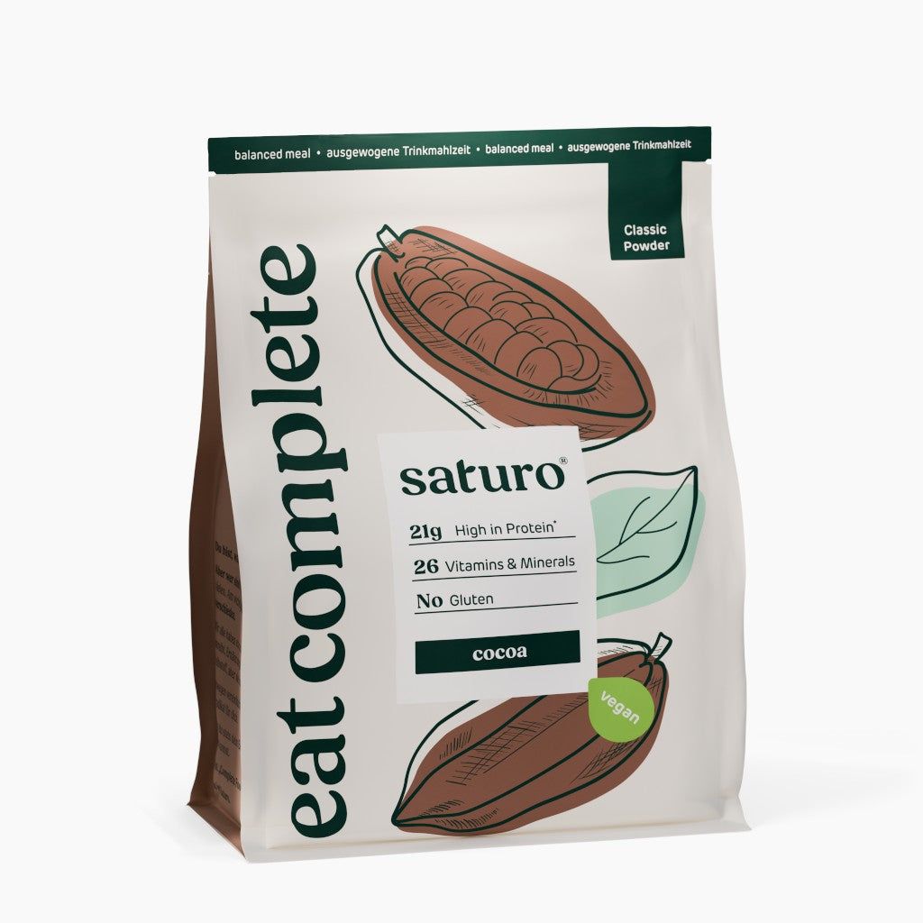 Beutel mit „eat complete“ und „saturo“. Enthält 21g Protein, 26 Vitamine & Mineralien, glutenfrei. Motiv: Kakaobohnen. Aufschrift: „vegan“.