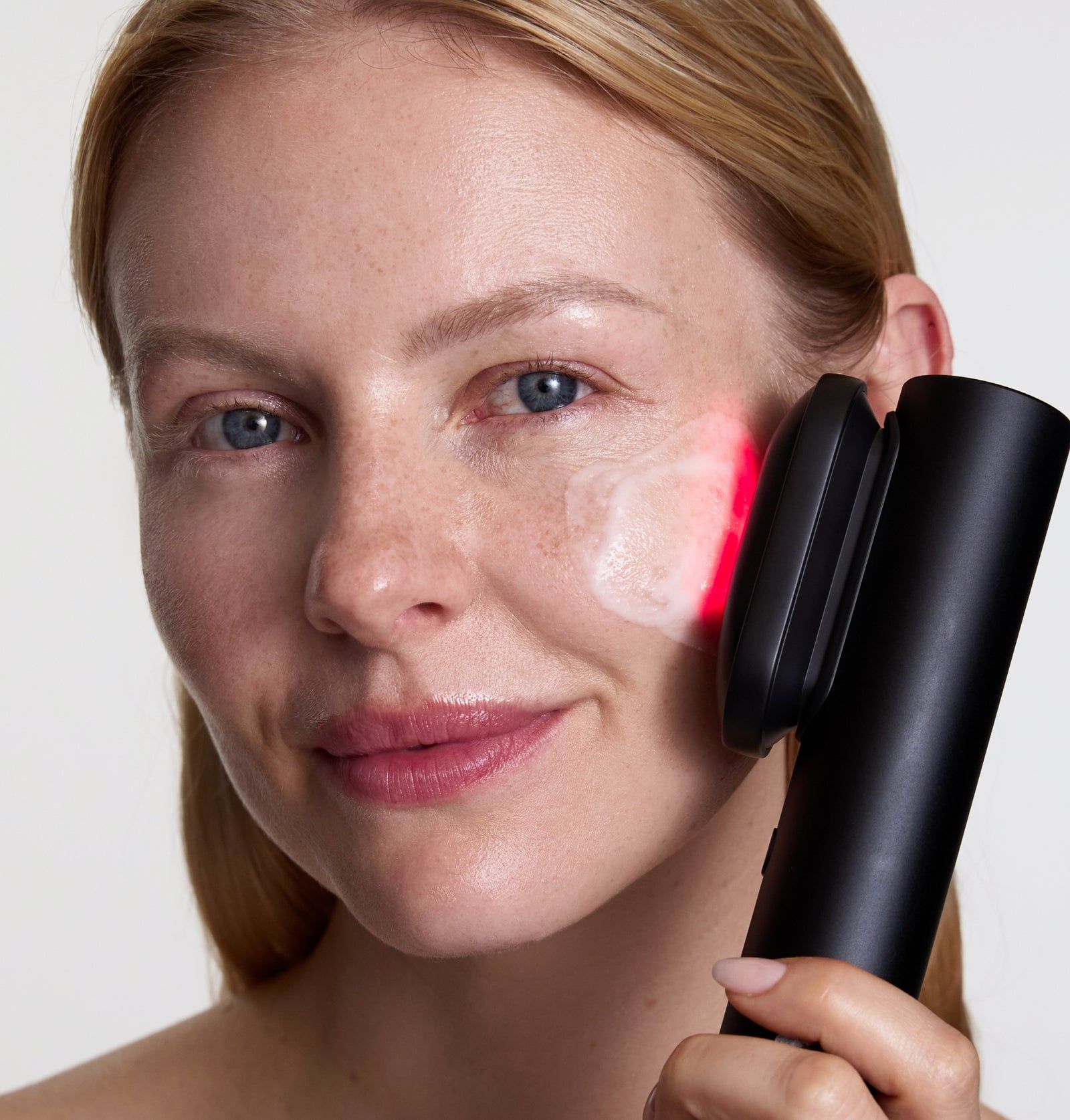 Frau mit BeautyDock+ an der Wange. Gerät mit rotem Licht. Schwarzes Gerät wird an der Haut angewendet.
