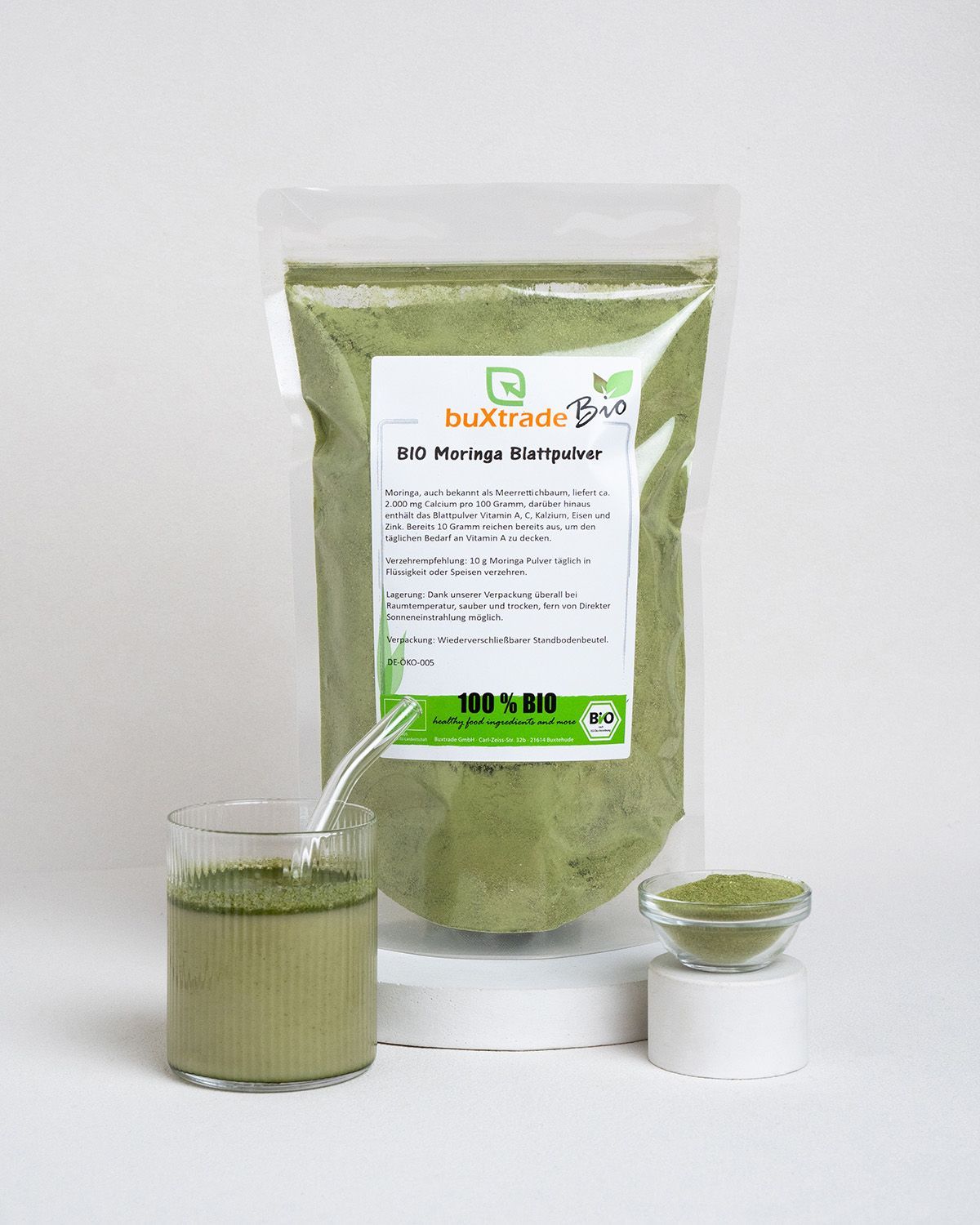 Glas mit grünem Getränk, Schale mit Pulver und Beutel mit Moringa-Pulver. Auf weißem Hintergrund.