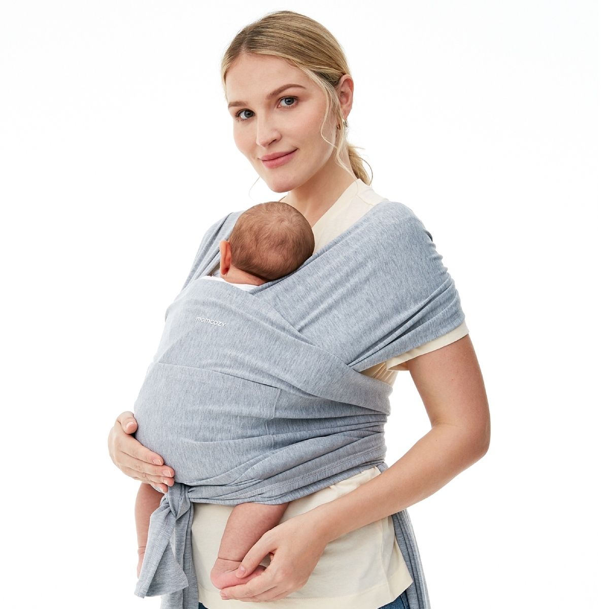 Ein hellgraues Momcozy Babytragetuch, das von einer Frau getragen wird, die ein Baby hält. Das Tuch ist um den Körper der Frau gewickelt und das Baby ist darin sicher gehalten. Das Momcozy-Logo ist auf dem Tuch sichtbar.