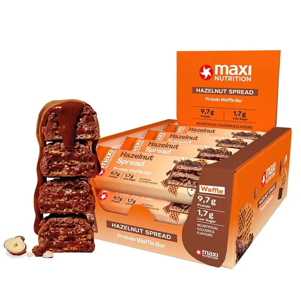 Protein Waffle Bar, Hazelnut Spread. Geöffnete Verpackung mit Riegeln. Einzelner Riegel mit Schokosauce. Haselnuss daneben.