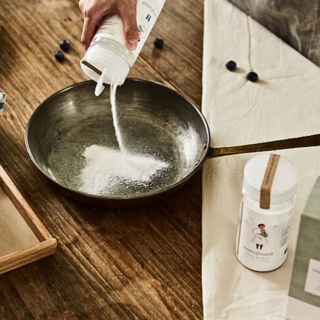 Person gießt Pulver aus Flasche in Pfanne. Flasche mit Etikett "Mighty Bubble Powder". Aufschrift: "Multi-Purpose Kitchen Cleaner".