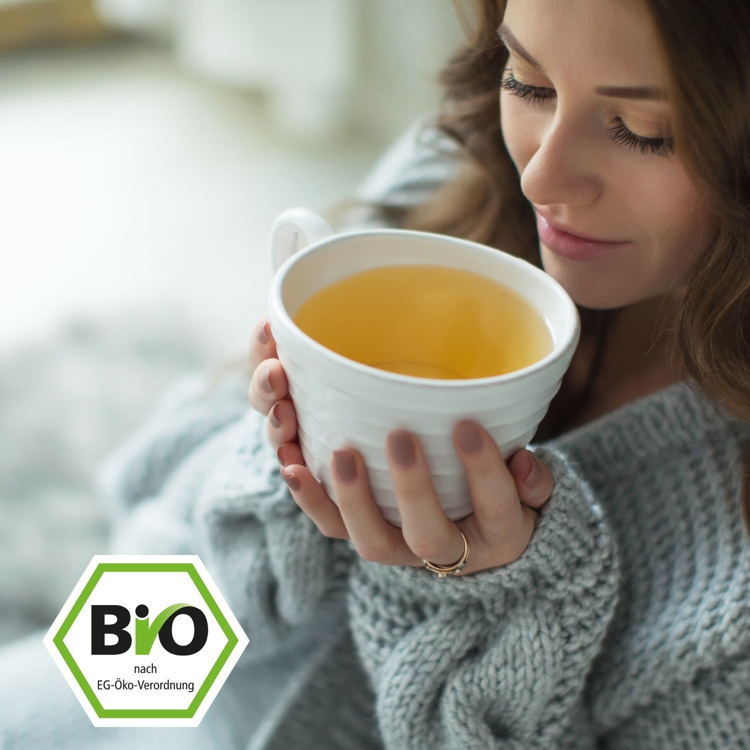 Frau hält eine weiße Tasse Tee. Bio-Siegel im Vordergrund.