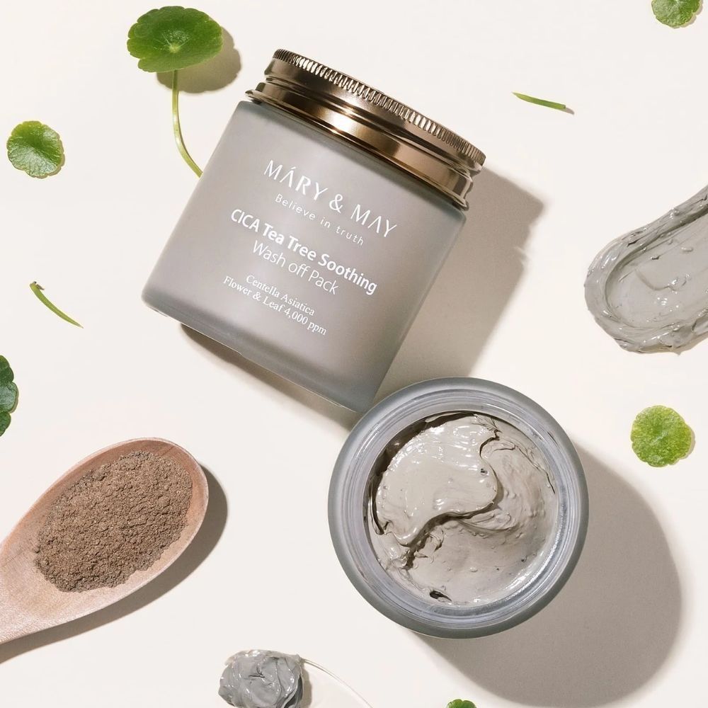 Mary & May CICA Tea Tree Soothing Wash off Pack, offener Behälter mit grauer Maske, daneben ein Holzlöffel mit Pulver.