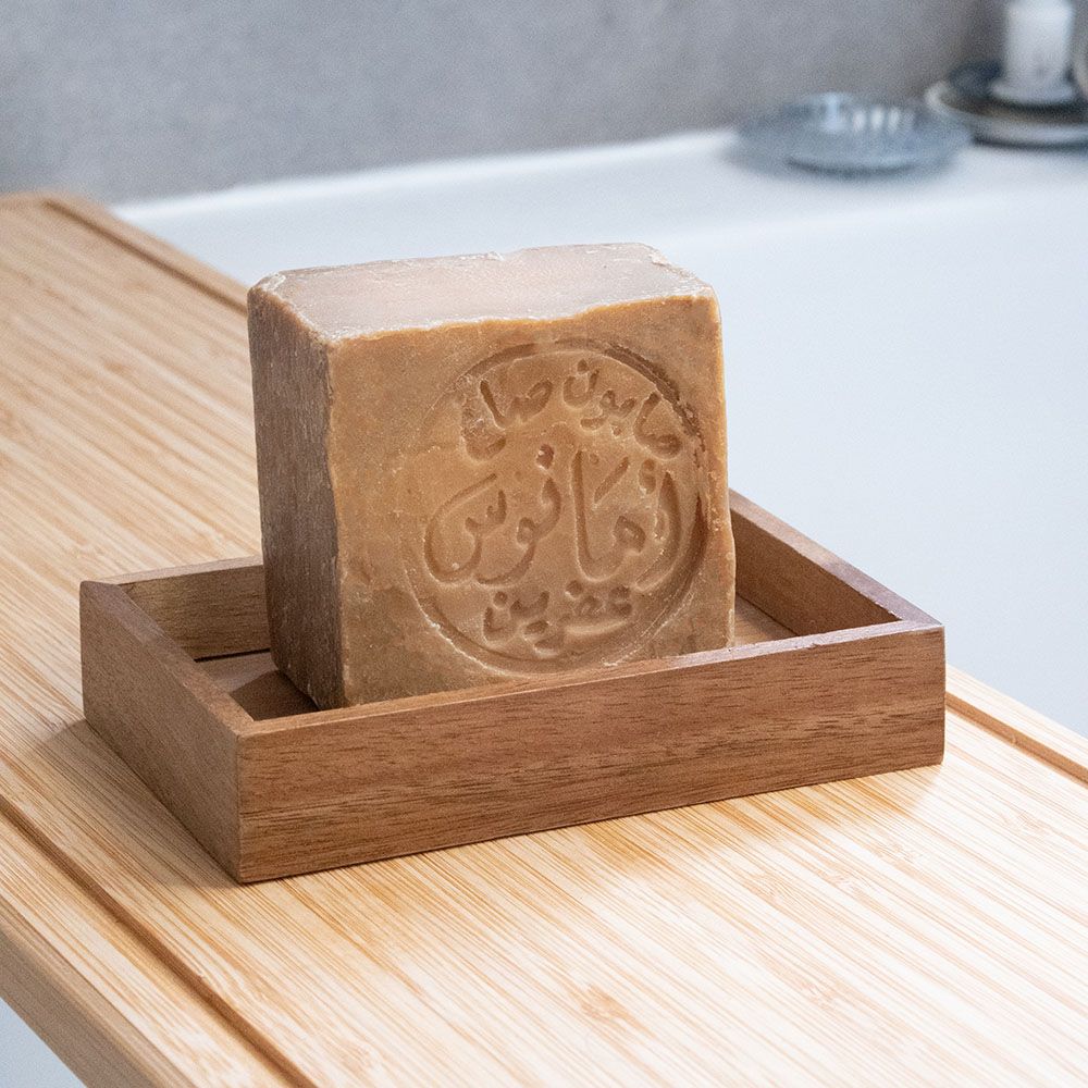 Ein Seifenstück, quadratisch, mit arabischer Schrift, in einer Holzseifenschale. Auf Holzbrett.