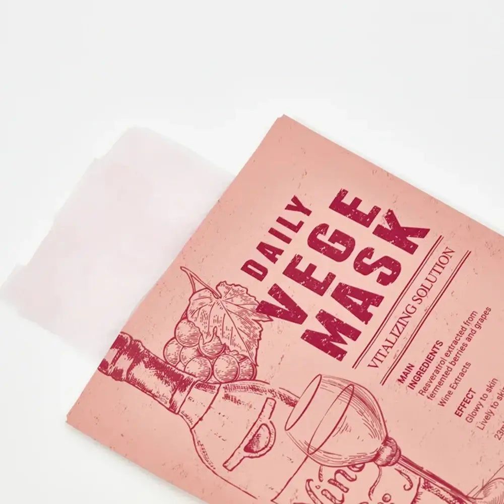 Rosa Maskenverpackung, teilweise geöffnet. Aufdruck: DAILY VEGE MASK, Wein-Illustration, Inhaltsstoffe, Wirkung. Weiße Maske sichtbar.