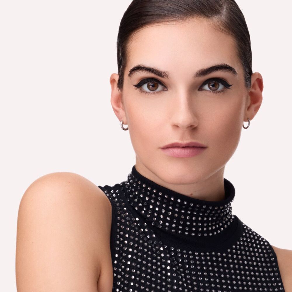 Porträt einer Frau mit schwarzem Eyeliner. Sie trägt ein schwarzes Oberteil mit Pailletten.
