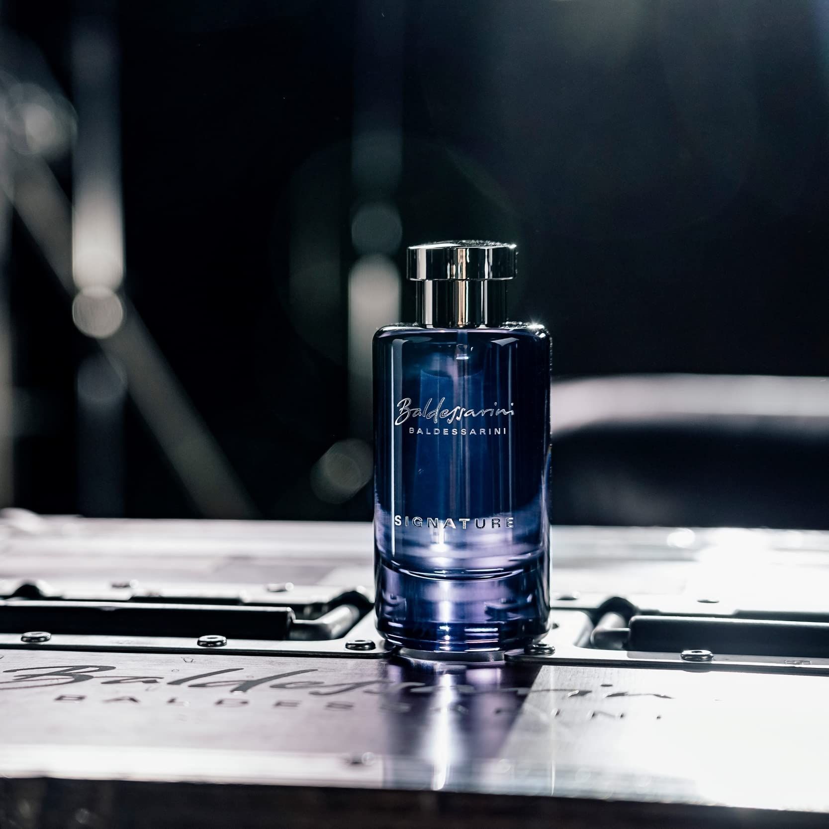 Dunkelblaue Glasflasche mit silbernem Verschluss auf metallischer Oberfläche.
