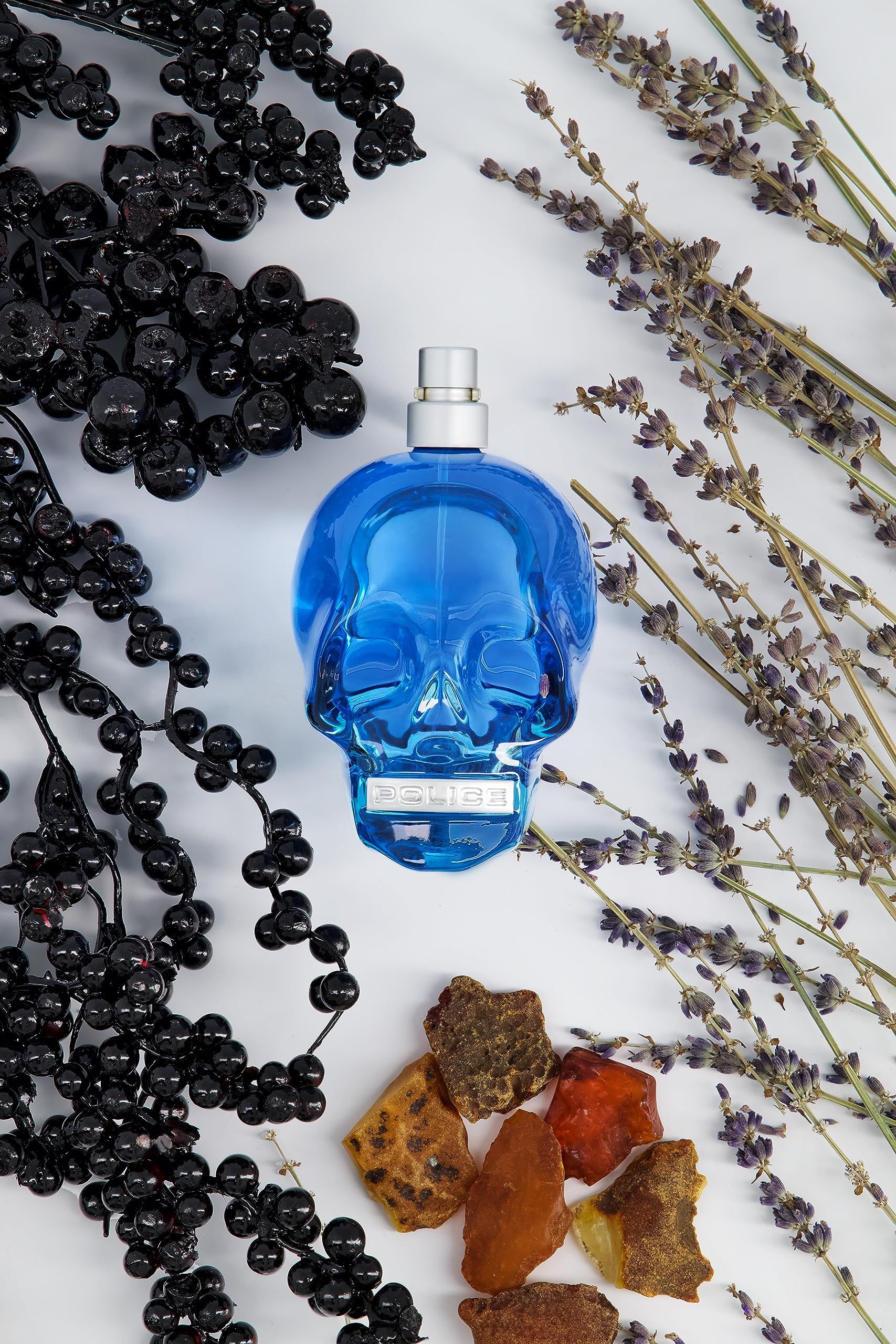 Blaues Parfüm in Totenkopf-Form. Umgeben von Beeren, Lavendel und Bernstein. Silberner Zerstäuber.
