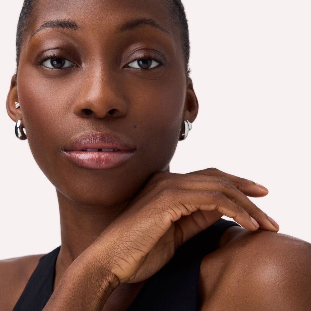 Porträt einer Frau mit dunkler Haut. Sie trägt silberne Creolen und hat glänzende Lippen.