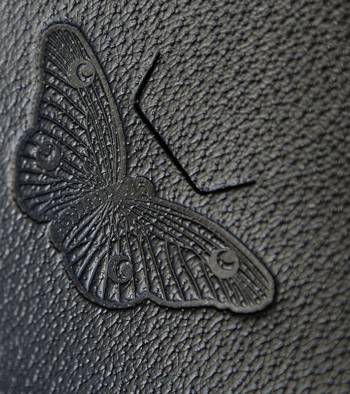 Schwarzes Leder mit geprägtem Schmetterlingsmuster. Detailaufnahme.