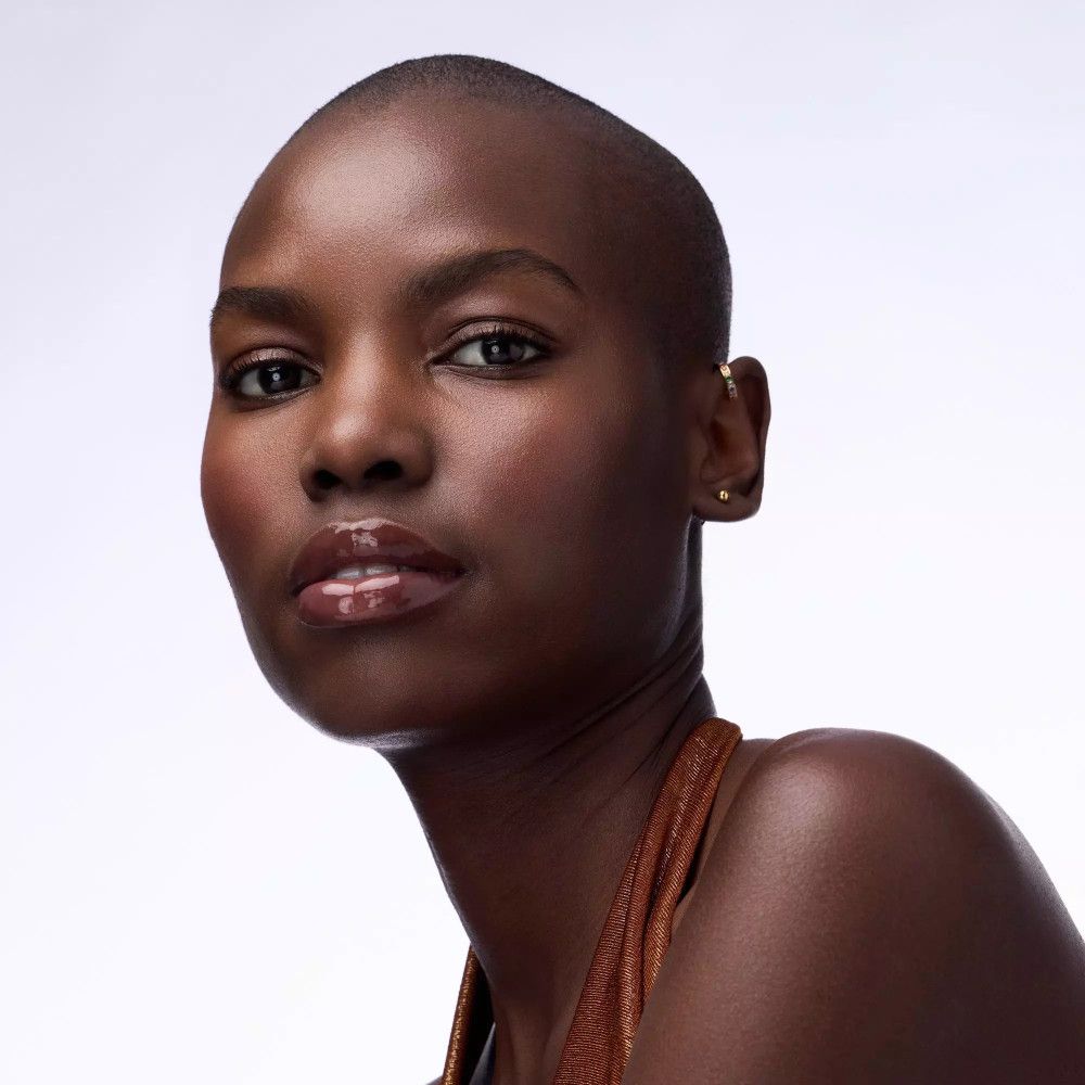 Porträt einer Frau mit dunkler Haut und rasiertem Kopf. Sie trägt Lippenbalsam.