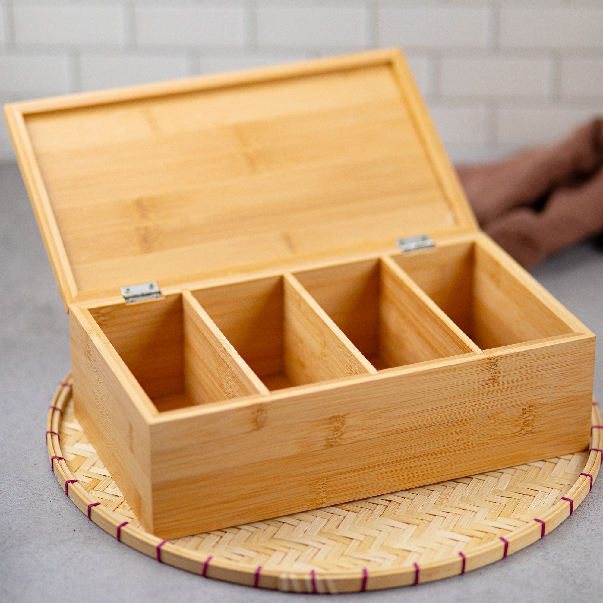 Geöffnete Holzbox mit vier leeren Fächern, auf einem geflochtenen Untersetzer platziert.