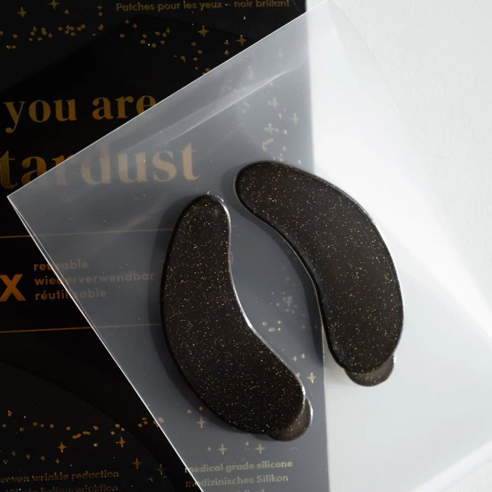 Zwei schwarze Glitzer-Augenpads in transparenter Verpackung. Aufschrift: "you are stardust".