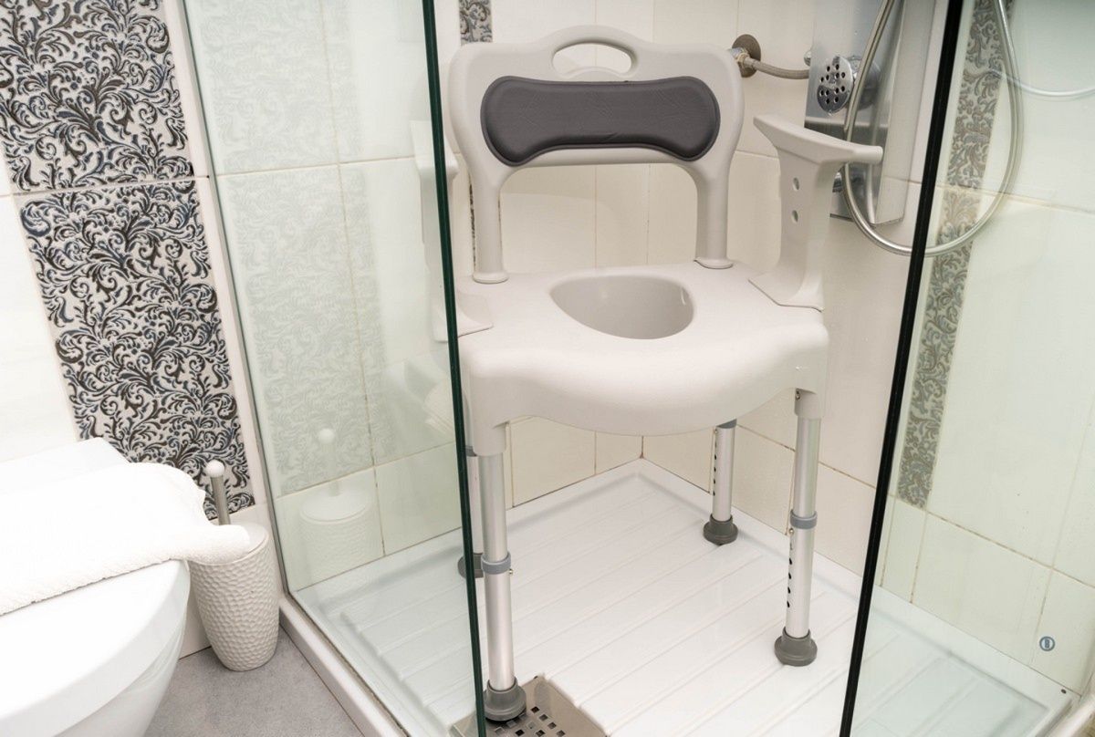 Dusch-WC-Stuhl in einer Duschkabine. Graue Sitzfläche und Rückenpolsterung. Weiße Struktur.