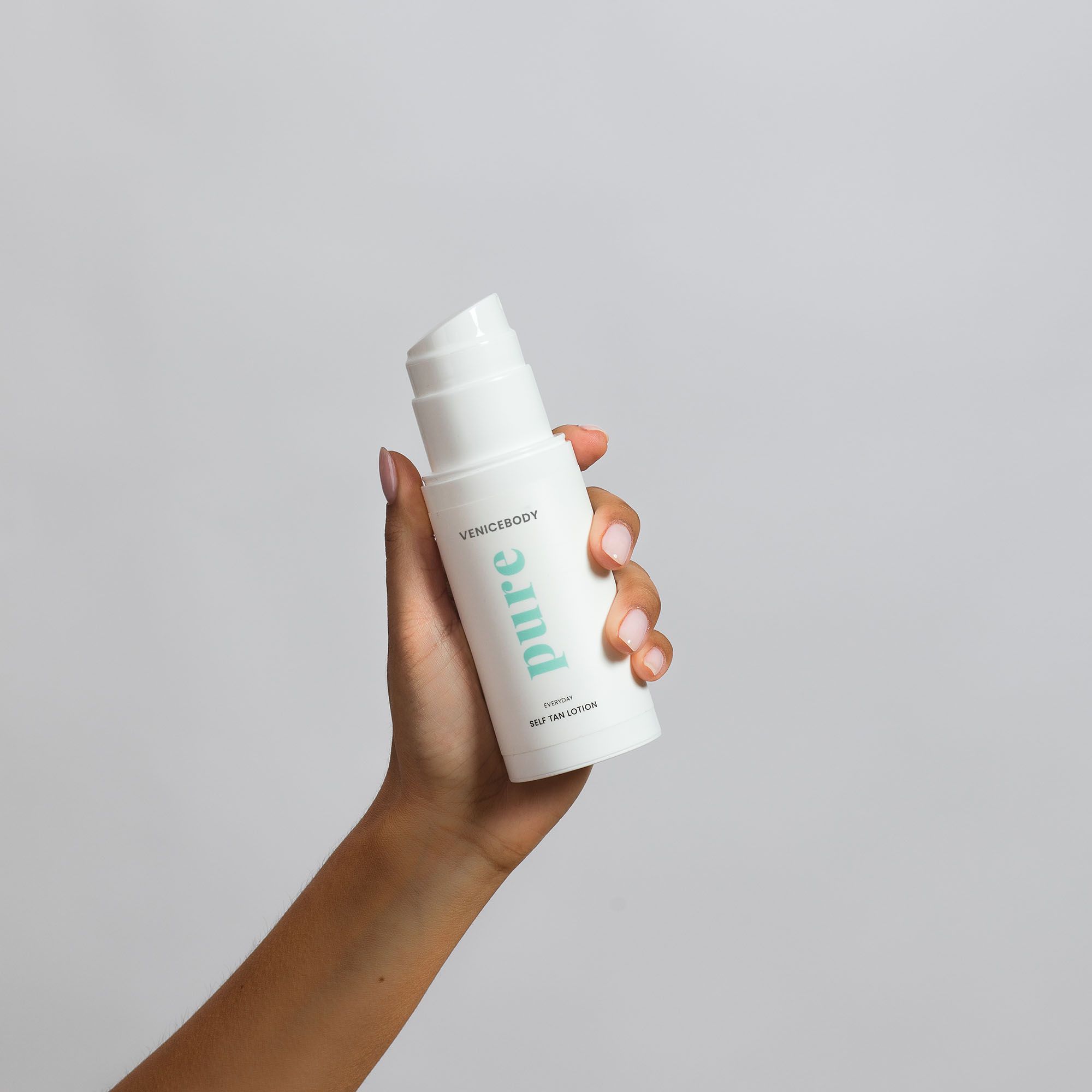 Weiße Flasche VENICEBODY pure Everyday Self Tan Lotion in einer Hand. Pumpkopf sichtbar.