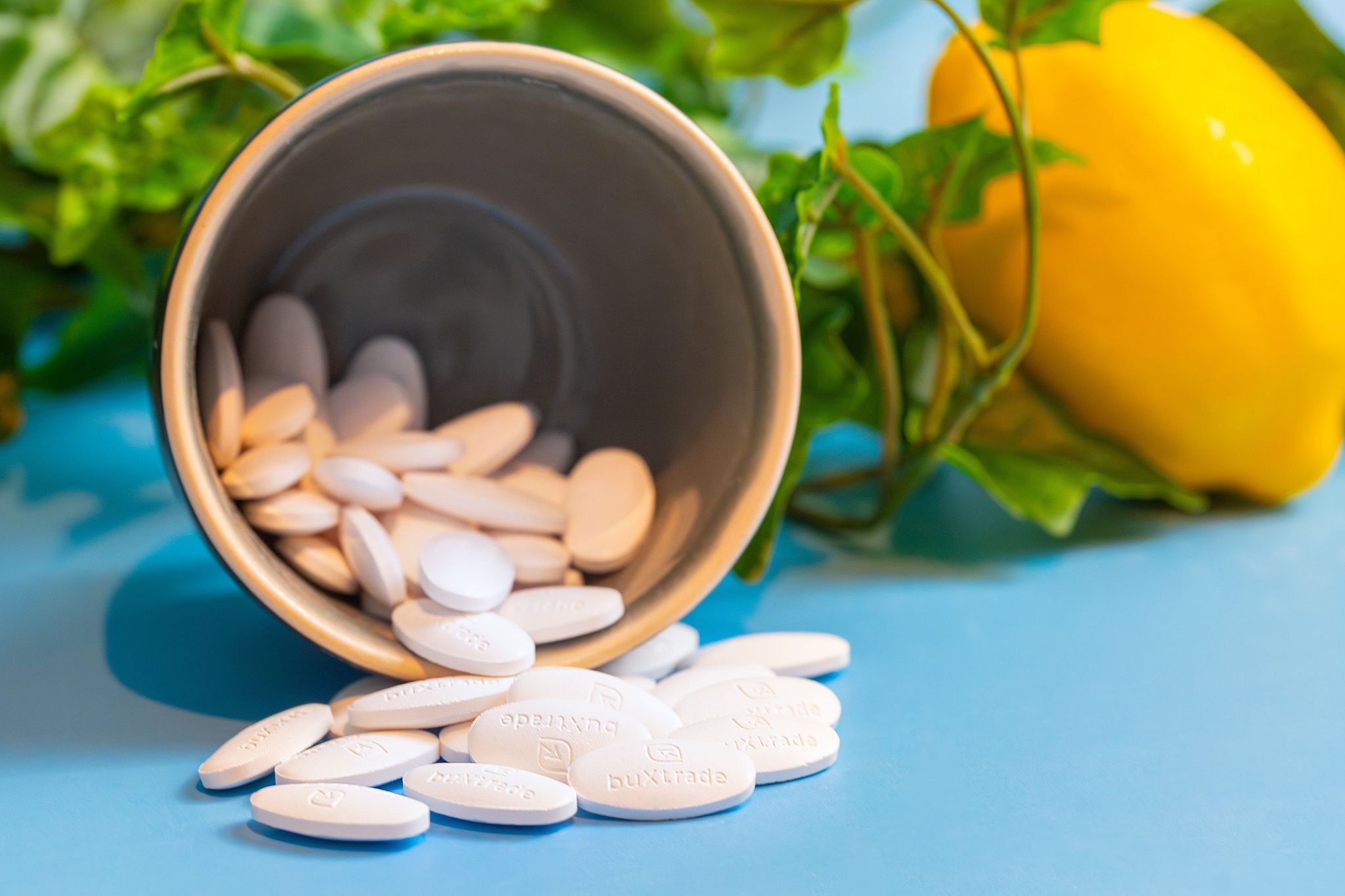 Tabletten liegen aus einem Becher. Einige Tabletten sind sichtbar. Im Hintergrund ein Zitronen- und Blattwerk.