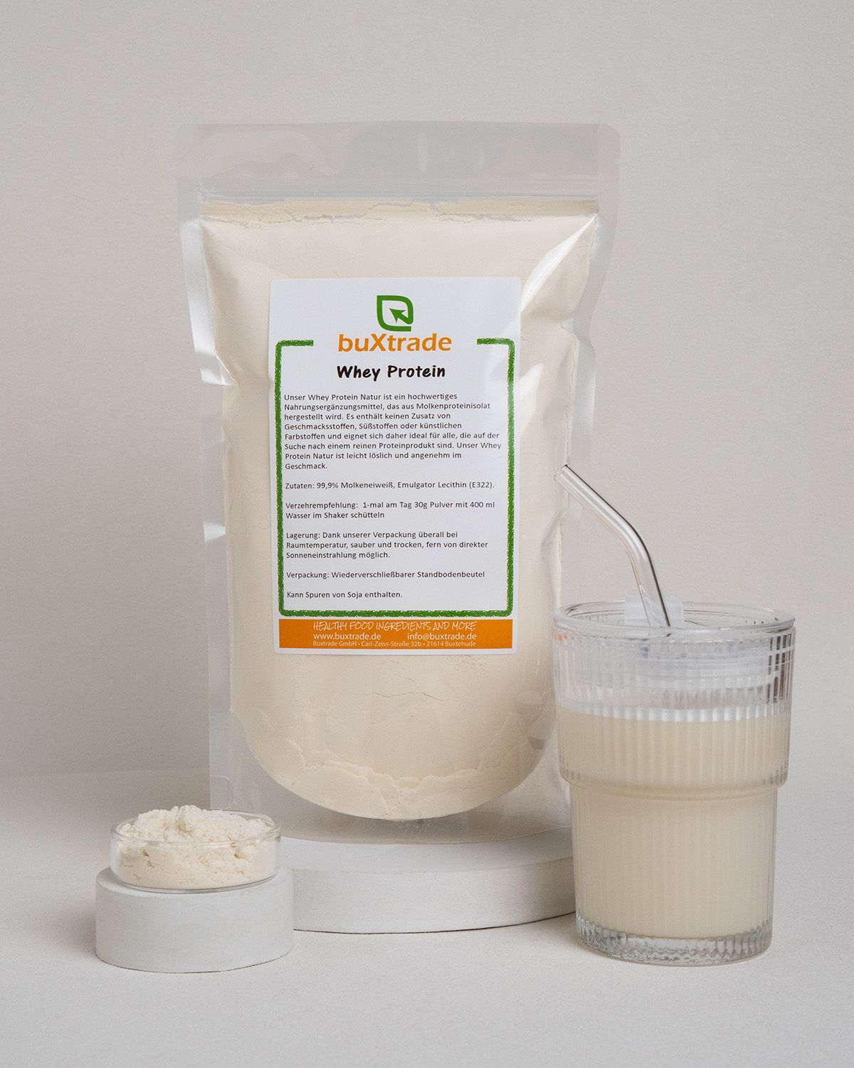 Verpackung mit Pulver, Glas mit Flüssigkeit und Strohhalm. Aufschrift: buXtrade Whey Protein.