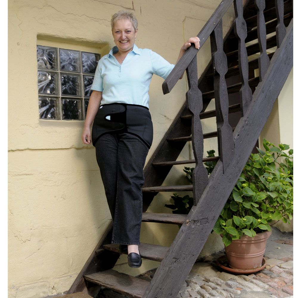Frau mit Hüftschutzgürtel auf einer Treppe. Schwarze Hose, hellblaues Oberteil.
