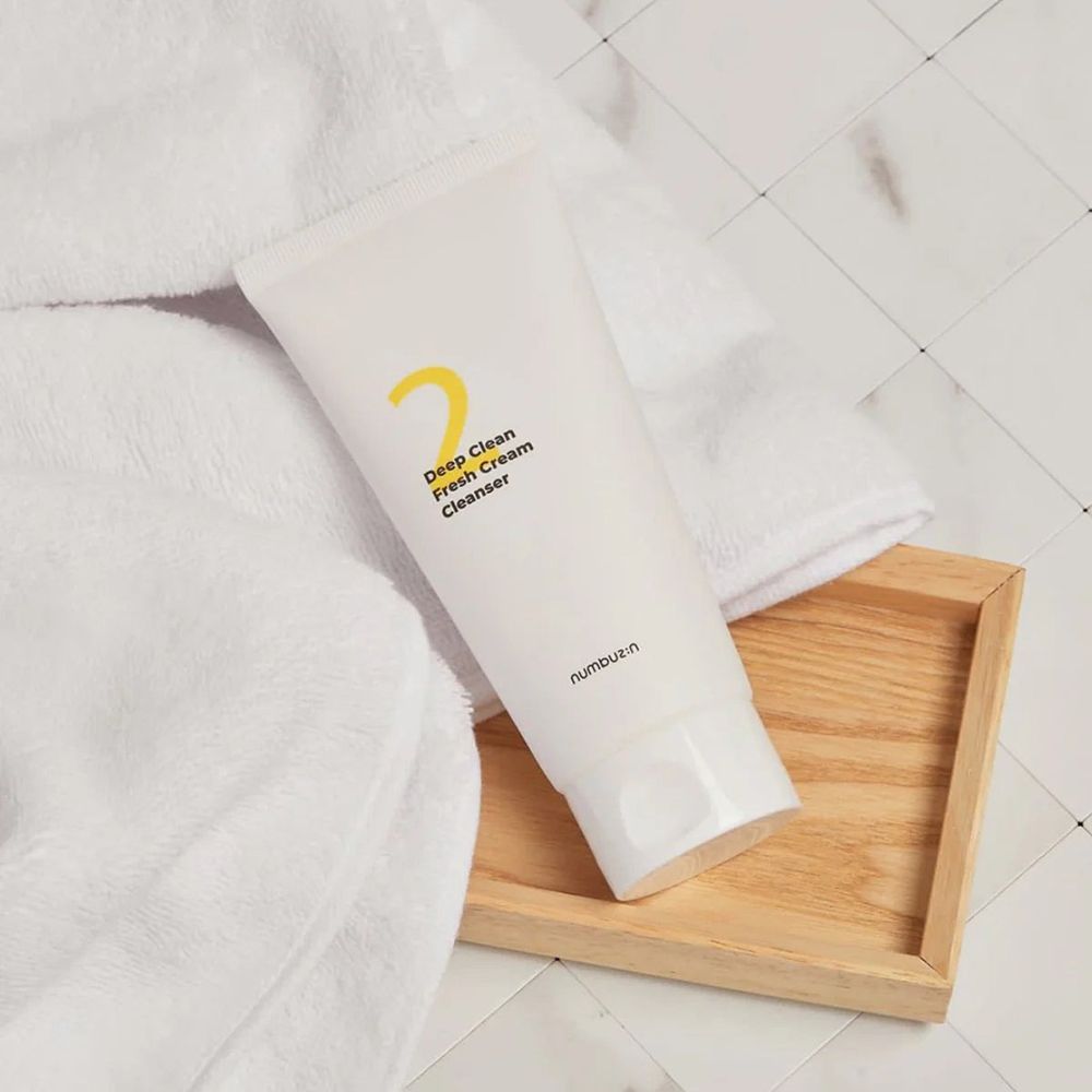 Weiße Tube auf einem Holztablett und weißem Handtuch. Aufschrift: "2 Deep Clean Fresh Cream Cleanser". Marke: numbuzin.