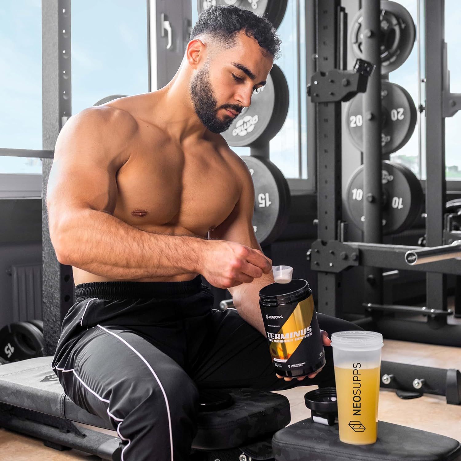 Mann in Fitnessstudio. Hält Dose und Shaker. Aufschrift: NEOSUPPS. Dose: TERMINUS Pre Workout Booster. Shaker mit gelbem Getränk.