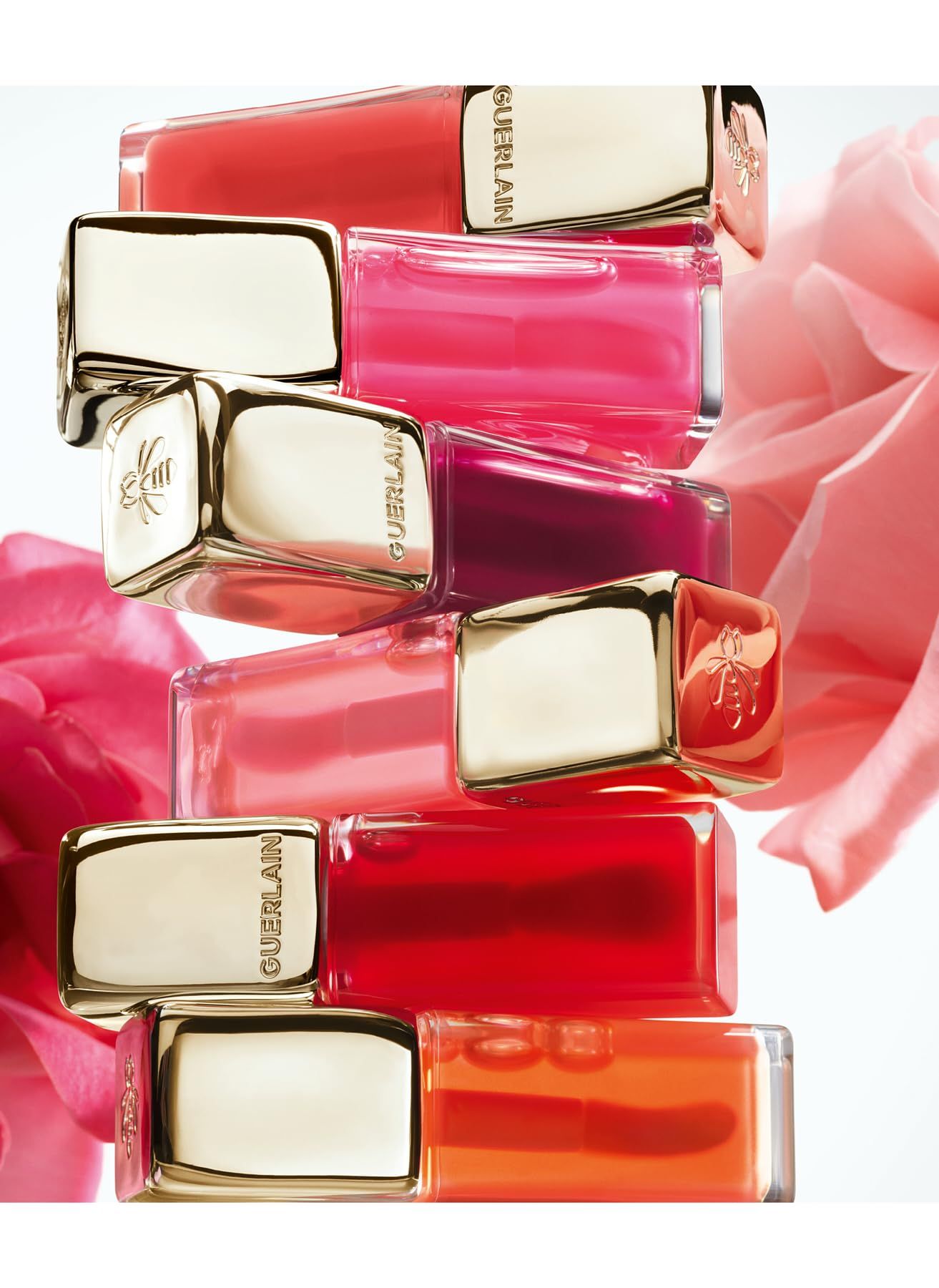 Mehrere Lippenstifte gestapelt. Goldene Kappen mit Logo. Verschiedene Farben. Hintergrund: rosa Blume.