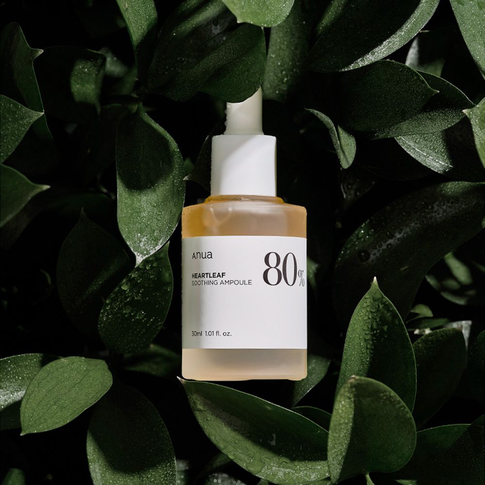 ANUA Heartleaf 80% Soothing Ampoule umgeben von grünen Blättern.