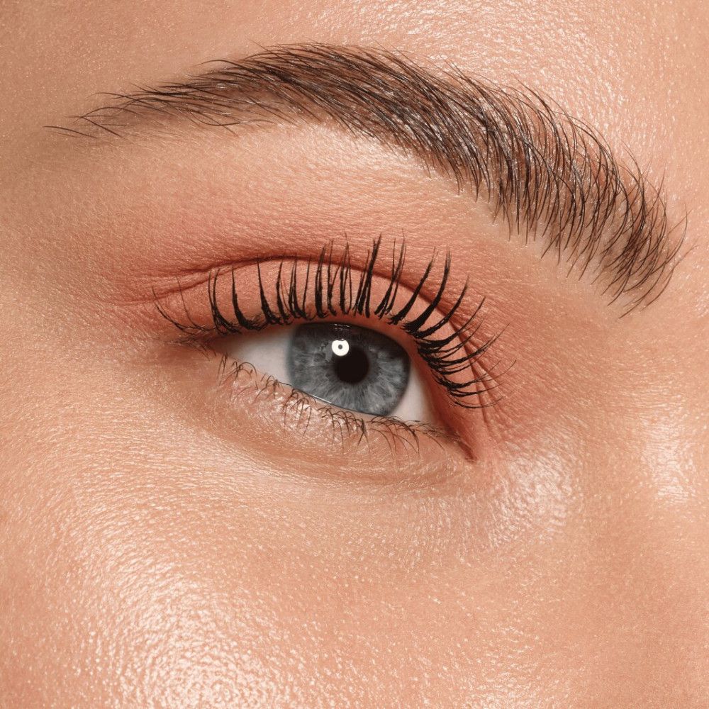 Nahaufnahme eines Auges mit rosa Lidschatten. Blaue Augen, dunkle Wimpern.