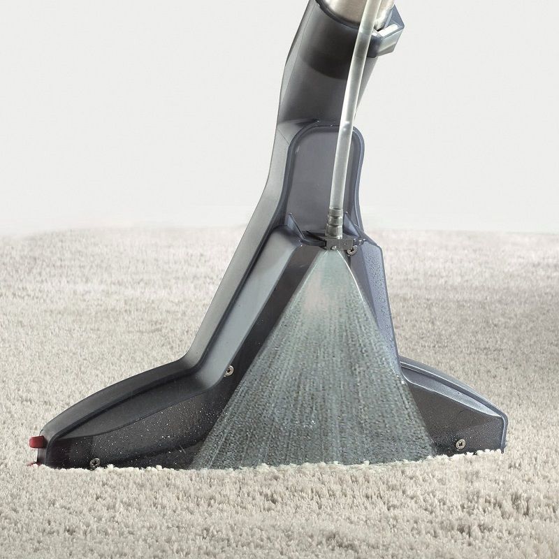 Düse sprüht Wasser auf Teppich. Schwarze Düse, grauer Teppich. Wasserstrahl sichtbar.