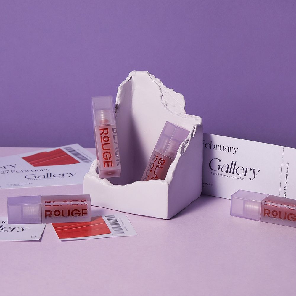 Mehrere Lippen-Gloss-Flakons. Auf weißem Podest. Hintergrund lila. Schriftzug BLACK ROUGE. Tickets.