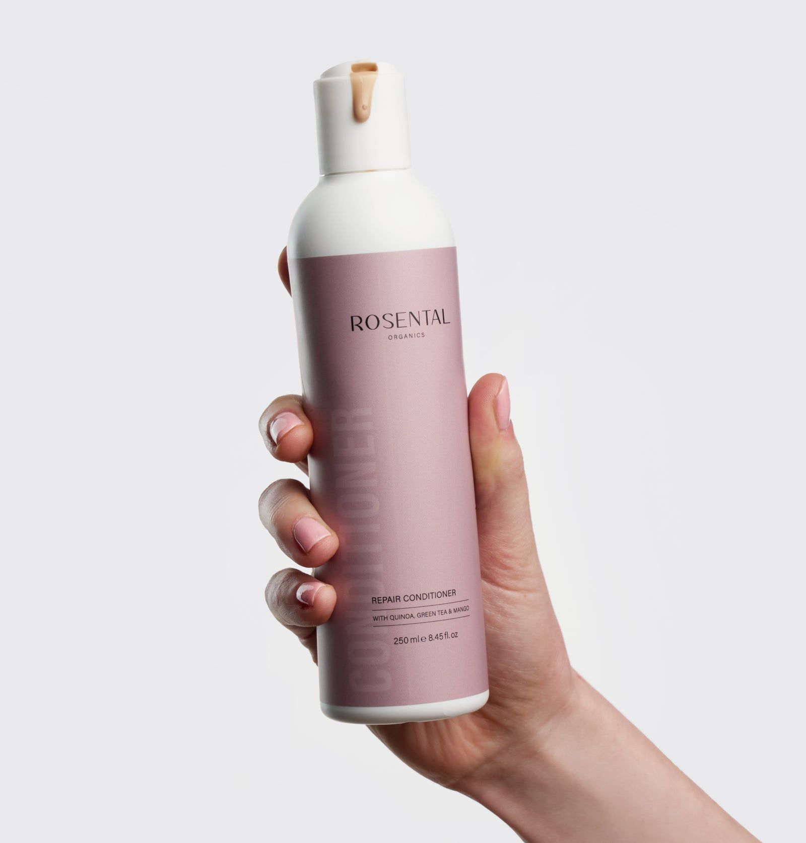 Eine Hand hält eine weiße Flasche mit rosa Etikett. Auf dem Etikett steht "Rosental Organics Repair Conditioner".