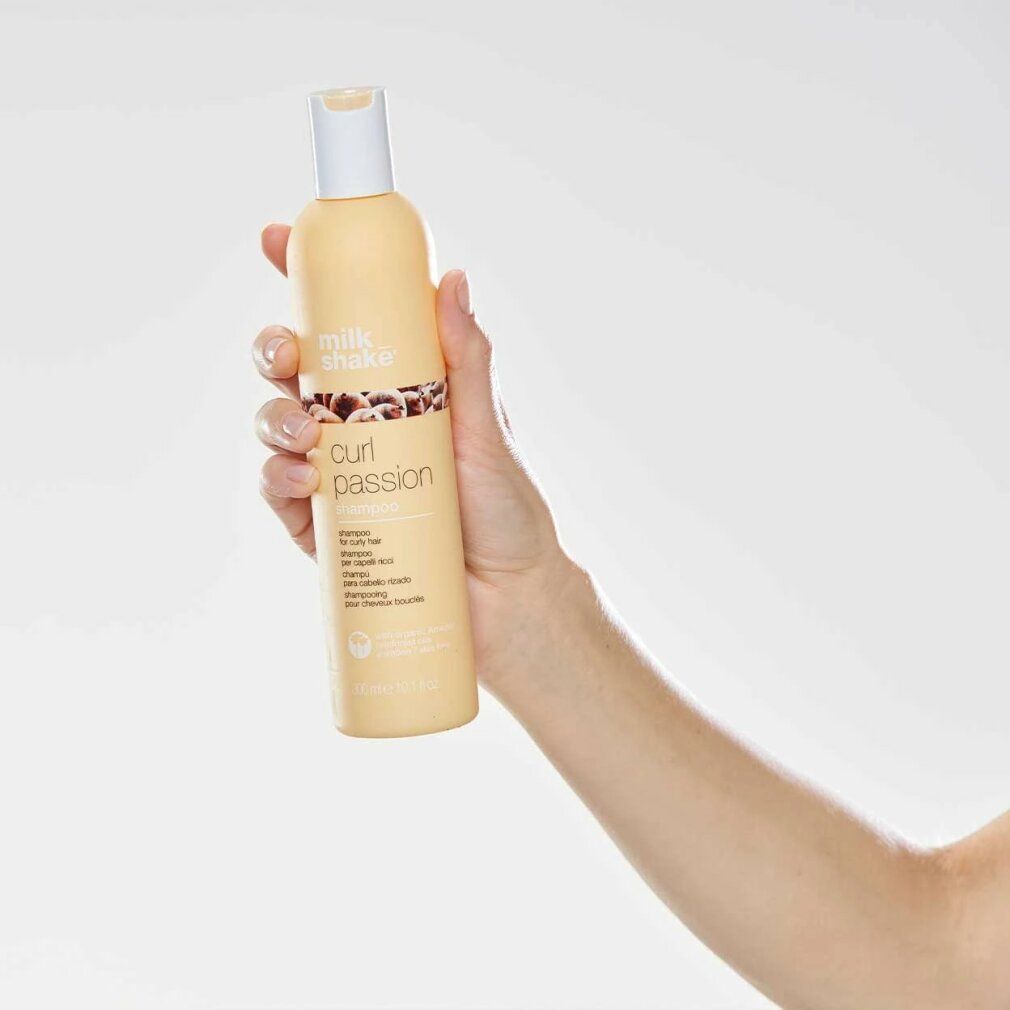 Beige Shampoo-Flasche, weißer Deckel, in Hand gehalten. Aufschrift: Milk Shake, Curl Passion. Für lockiges Haar.