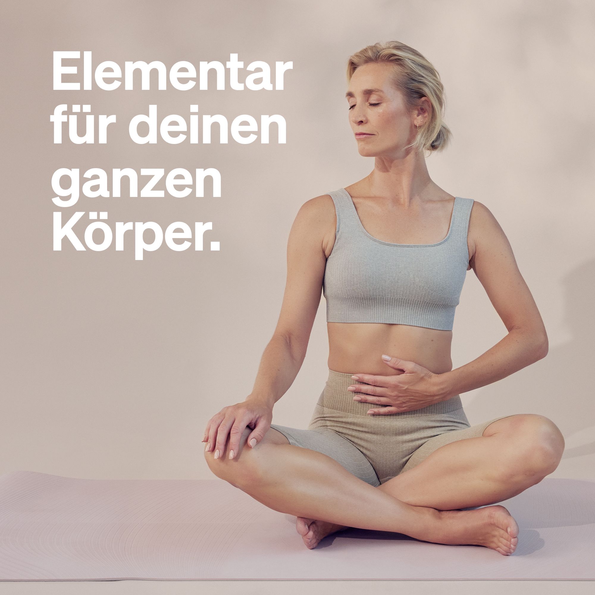 Frau sitzt auf einer Yogamatte, Hände auf dem Bauch. Text: Elementar für deinen ganzen Körper.