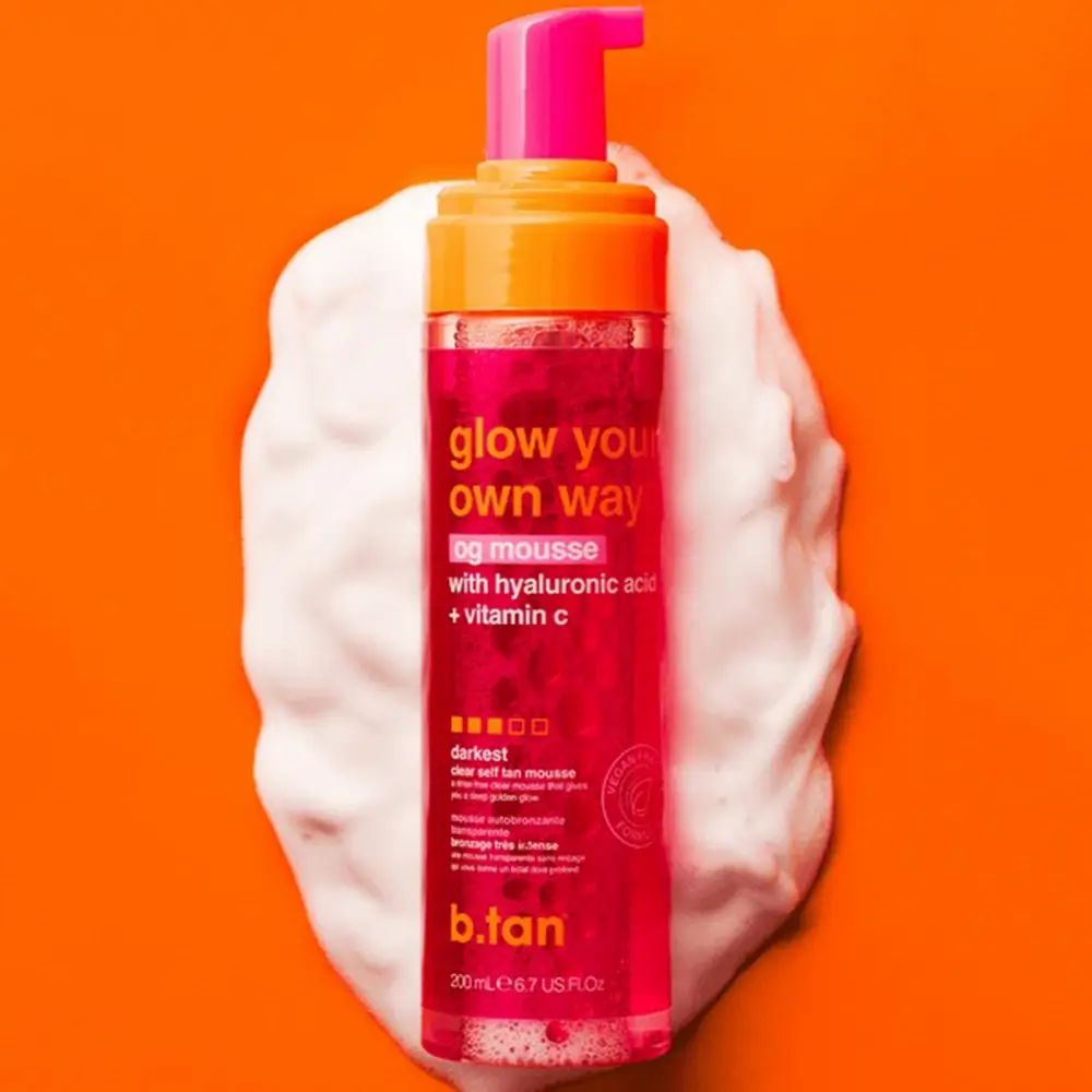b.tan Selbstbräunungs-Mousse in einer durchsichtigen Flasche mit orangefarbenem Pumpaufsatz und rosa Akzenten. Enthält Hyaluronsäure und Vitamin C.