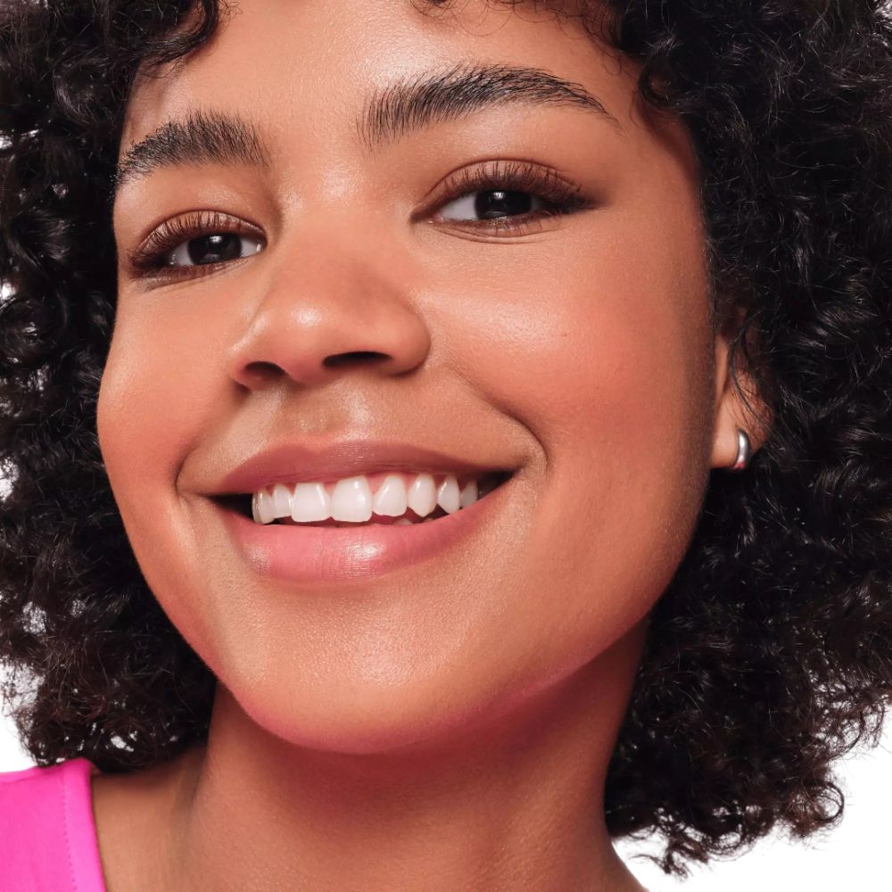 Nahaufnahme eines lächelnden Gesichts mit Locken und Ohrring. Sie trägt Make-up.