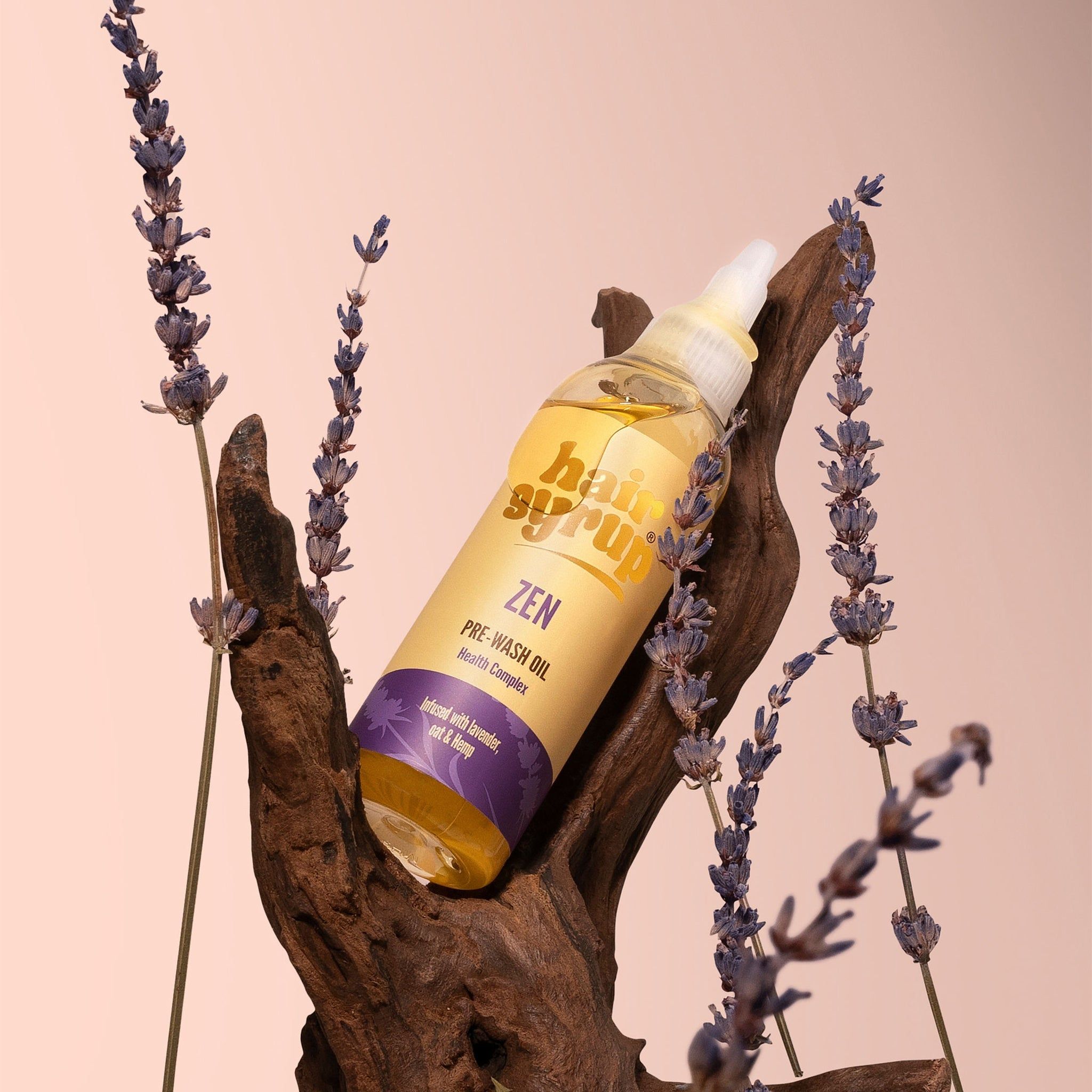 Eine Flasche mit gelber Flüssigkeit, Etikett mit Text. Die Flasche liegt auf einem Stück Holz, umgeben von Lavendel.