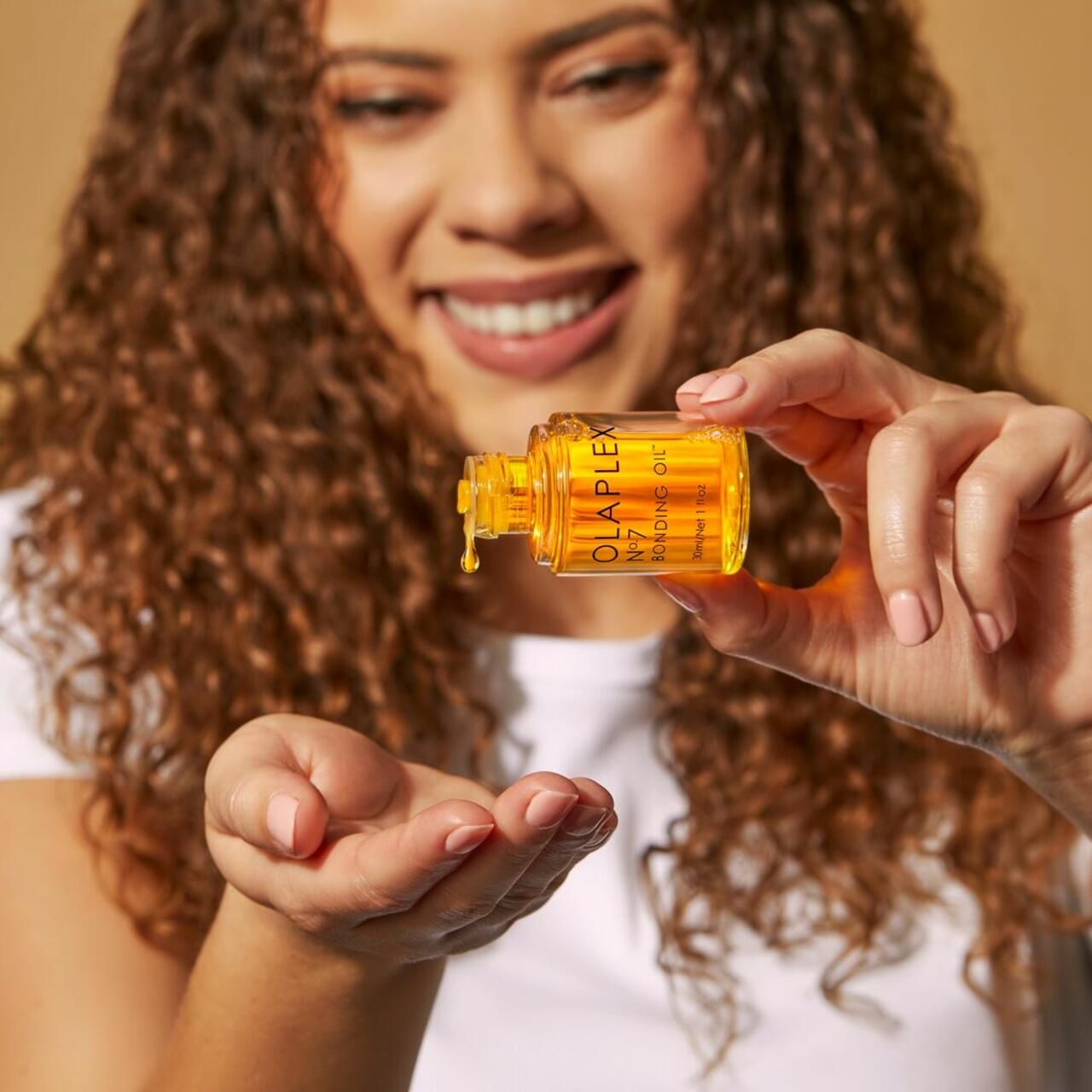 Person hält eine kleine Flasche Olaplex No.7 Bonding Oil. Öl tropft in die Handfläche.
