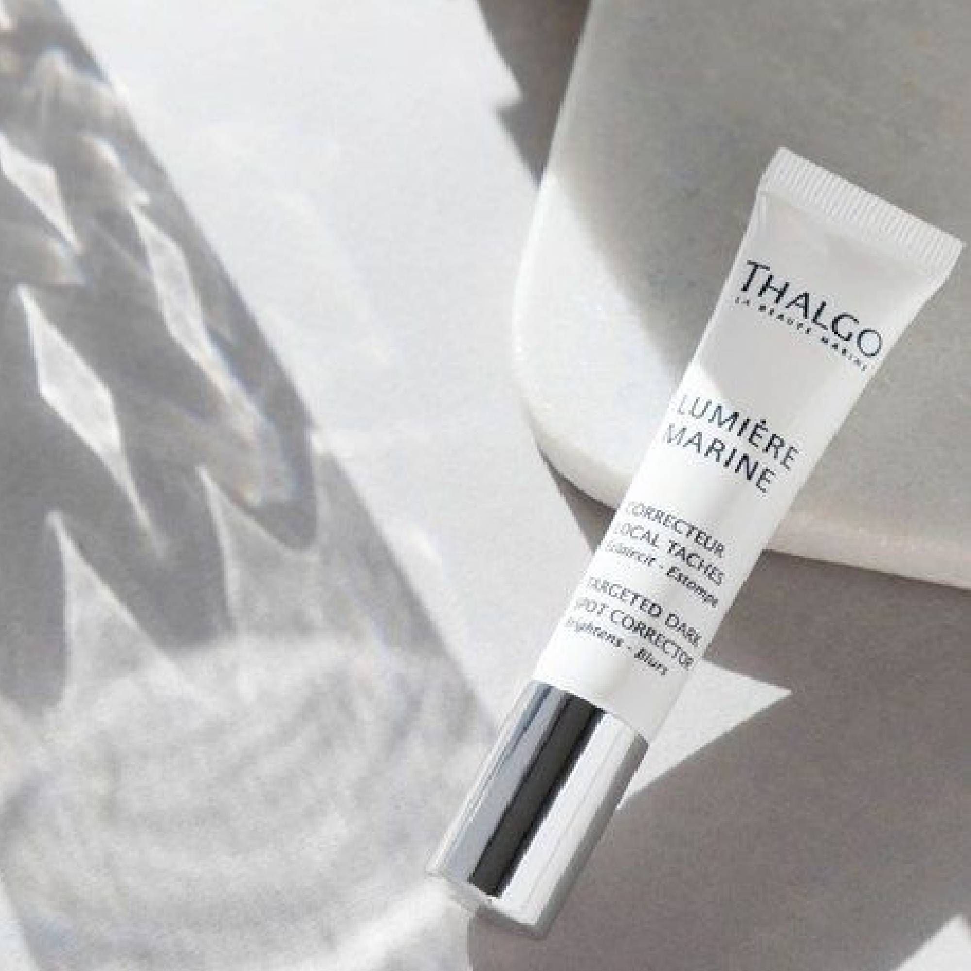 Weiße Tube mit silbernem Verschluss. Aufschrift: THALGO, LUMIÈRE MARINE, Korrekturstift gegen Pigmentflecken. Auf hellem Untergrund.