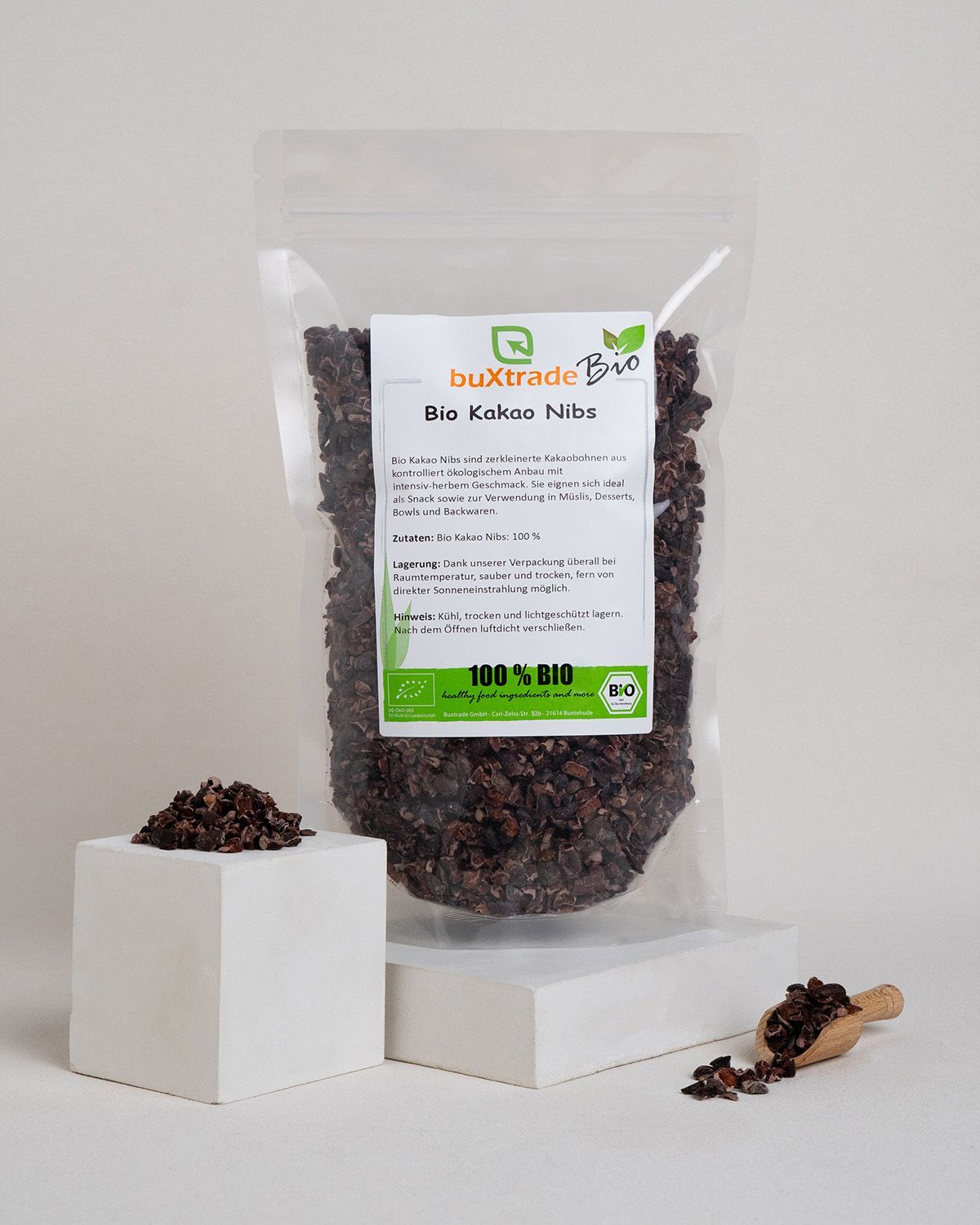 Verpackung mit Bio Kakaonibs, daneben ein Würfel mit Kakaonibs und eine Holzschaufel.