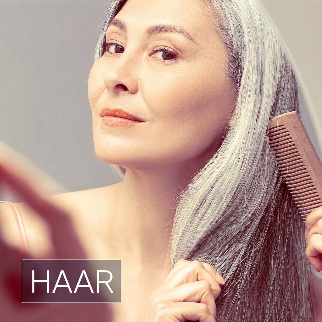 Eine Frau mit langen, grauen Haaren kämmt ihr Haar mit einem Holzkamm.