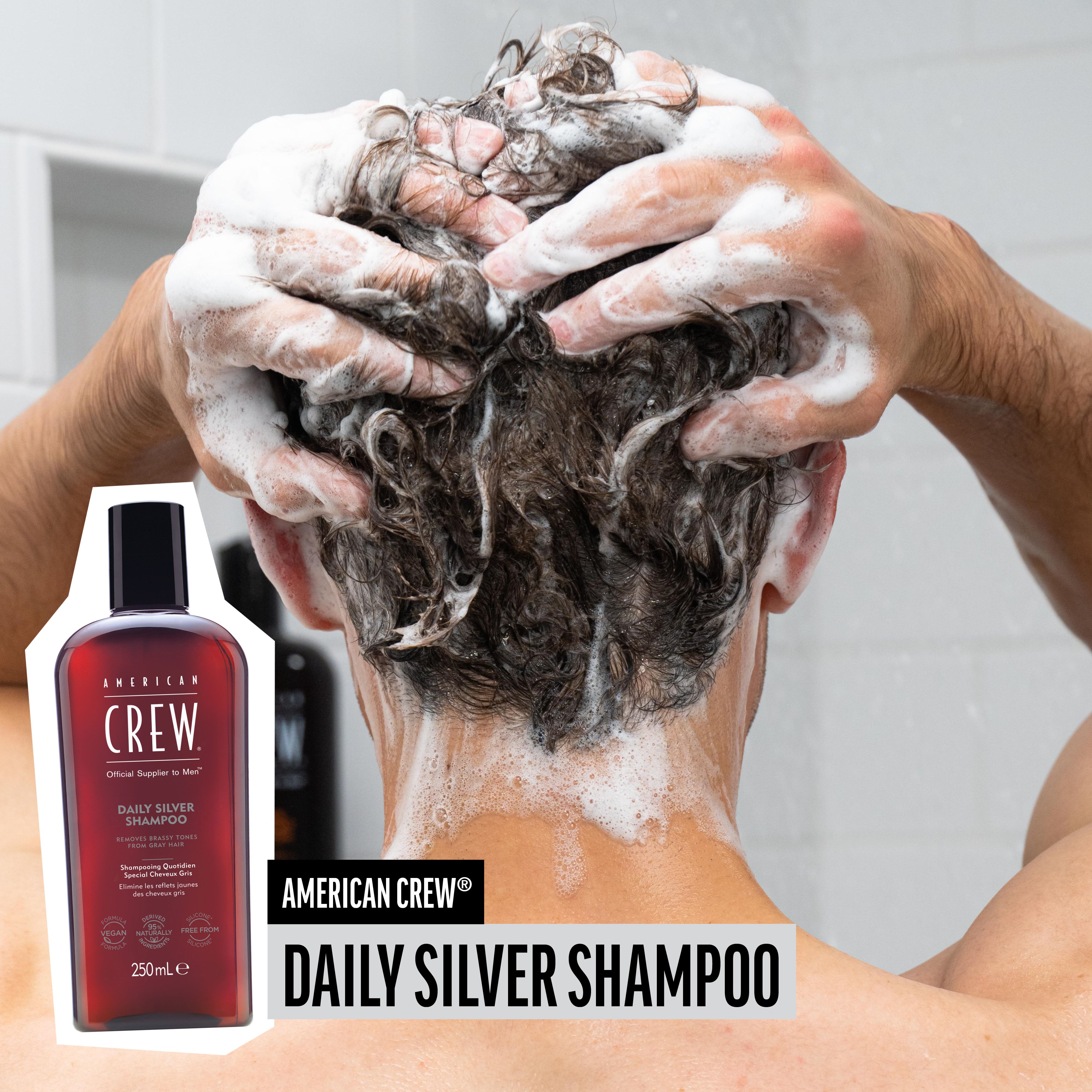 Mann wäscht sich die Haare mit AMERICAN CREW Daily Silver Shampoo. Shampoo-Flasche im Bild. Schaum auf dem Kopf.