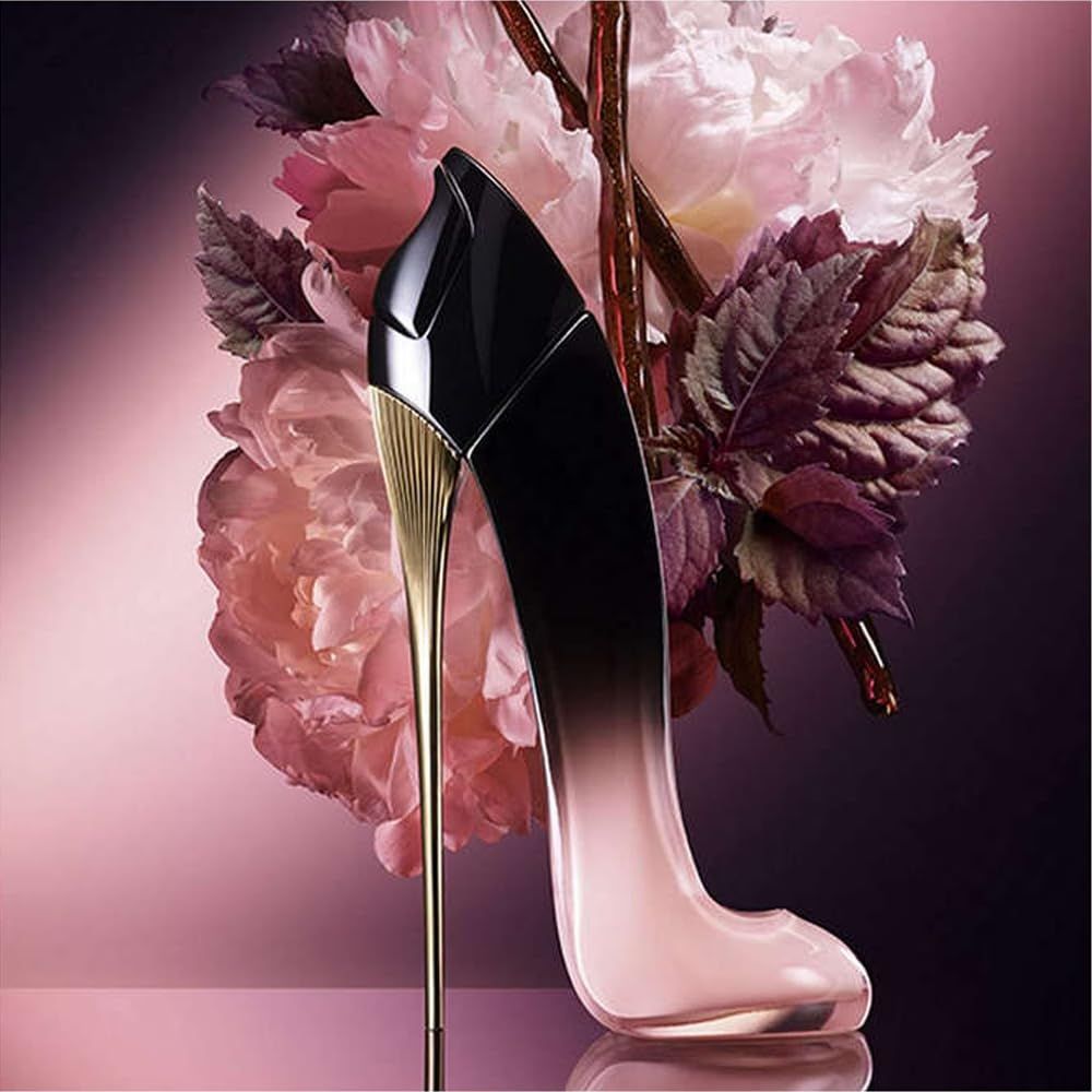 Parfümflakon in Schuhform. Schwarz-rosa Farbverlauf, goldfarbener Absatz. Vor rosa Blüten platziert.