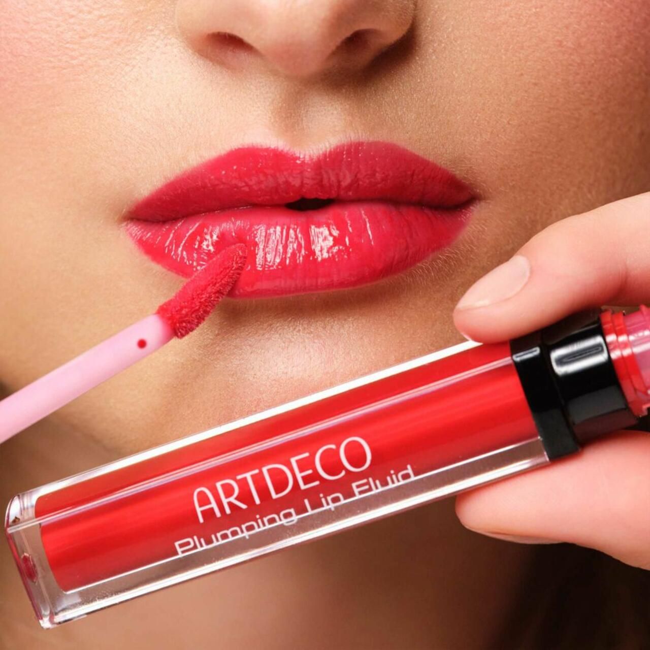 Artdeco Plumping Lip Fluid wird auf Lippen aufgetragen. Rote Lippen, Produkt und Applikator sichtbar. Produktname.