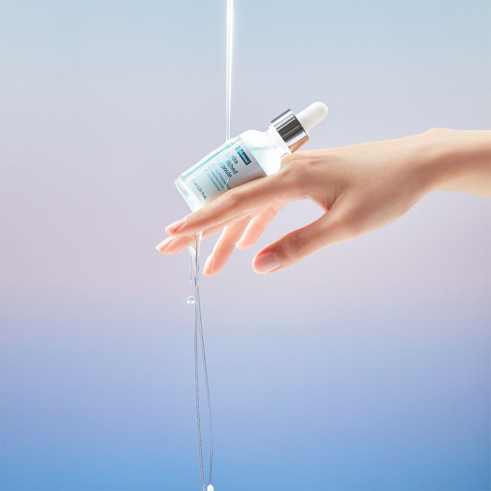 Hand hält Serumflasche. Flüssigkeit fließt aus der Flasche. Blauer und weißer Hintergrund.