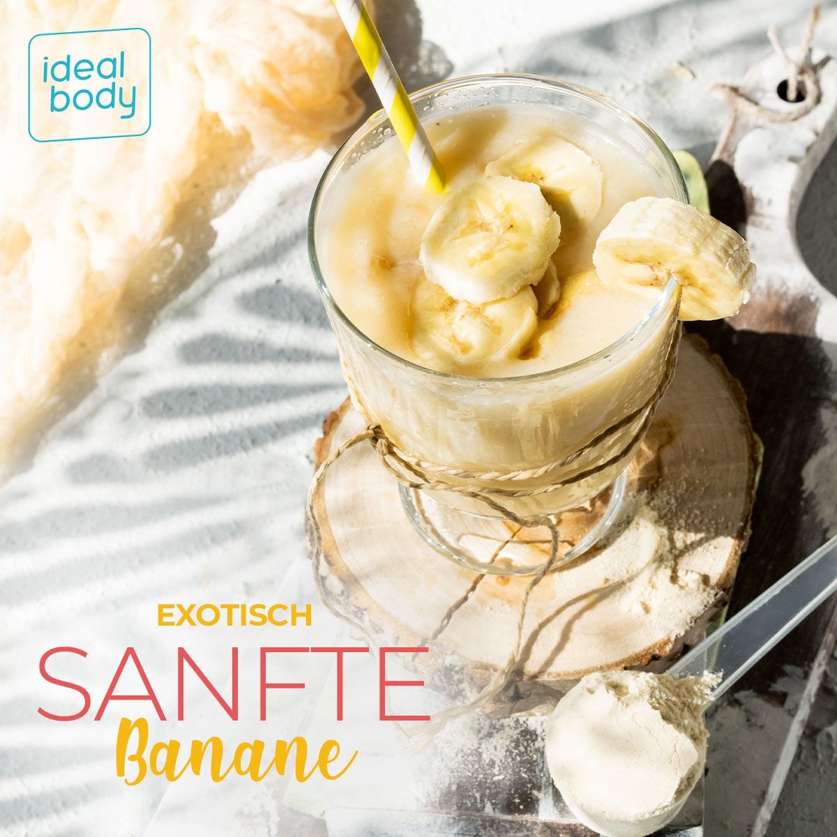 Glas mit Bananenshake, Bananenscheiben und Strohhalm. Auf Holzuntersetzer. Löffel mit Pulver daneben. Text: Exotisch Sanfte Banane.