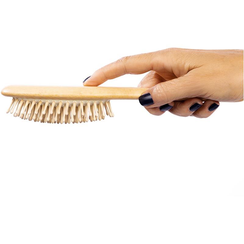 Eine Hand hält eine ovale Holzbürste mit hellen Holzstiften. Die Bürste liegt horizontal. Der Hintergrund ist weiß.